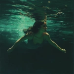**Swimmer gliding just below the surface, long hair flowing, muted moonstone emerald and sand-colored light with subtle golden caustics, peaceful and quiet." --profile fbik8zy --v 7.0** - Upscaled by <@997706764311089183> (fast)