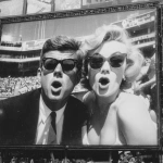 **a high resolution black and white photograph of JFK in 1961 wearing Ray Ban wayfarer sunglasses and caught on a "kiss cam" on a stadium Jumbotron with Marilyn Monroe, also in Ray ban wayfarer sunglasses; both have a look as if they are surprised they just got caught** - Image #2 <@728020337156948019>