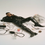 **advertising shot of balenciaga, white background. a man wearing black and high boots is lying on the ground with his phone in hand, making a call while holding bags from balenciaga, surrounded by cables, coffee cups, and glasses. the scene was designed in the style of john galliano for vogue magazine. it's a masterpiece! --ar 9:16 --v 7.0** - Upscaled by <@1140324697154797598> (fast)