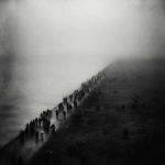 **An evocative and minimalist digital artwork, wide aerial shot, with a dark, monochromatic aesthetic, maintaining the style of the previous designs. The composition depicts a vast, dense crowd of silhouetted figures moving along a narrow strip of land, bordered by a muted, dark sea on one side and a barren, shadowy landscape on the other. The sheer number of individuals creates a sense of overwhelming displacement. The sky is overcast and a uniform dark tone, contributing to a feeling of somberness and uncertainty. The figures appear small and almost indistinguishable, emphasizing the scale of the exodus and their collective vulnerability. The scene evokes a powerful sense of forced migration and the loss of place, rendered with a stark and uncluttered visual style** - Image #3 <@1032195406119043132>