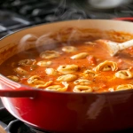 **Creamy tomato tortellini soup cooking in a large red Dutch oven on a stovetop, rich tomato base bubbling gently with cheese tortellini floating, steam rising, wooden spoon resting on the side, soft kitchen lighting, cozy evening cooking atmosphere --v 6.0 --ar 4:5 --raw** - Image #2 <@1321895242076520463>