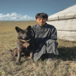 **<https://s.mj.run/o_yLqhTb4aU> <https://s.mj.run/6fMYZkMLVic> A teenage boy sitting next to a dark-colored German Shepherd dog near a traditional Mongolian yurt on grassland, wearing traditional Mongolian casual clothing, the dog wearing a decorative collar around the dog's neck similar to reference image, scattered wildflowers on the prairie, shot with iPhone camera, midday lighting, natural sunlight, portrait photography, vertical composition --ar 2:3 --iw 1.5 --v 7.0** - Image #3 <@366883290000392193>