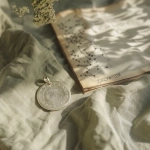 **A handcrafted silver pendant with engraved angel numbers, placed gently on a pale sage green linen cloth. Behind it, a faded hand-drawn star chart sketch is partially visible on kraft paper. Natural morning light spills diagonally, creating subtle warmth. Color palette: pale green, linen white, silver, hint of golden hour. Mood: modern mystic, soft and grounded. --v 6.0** - Image #1 <@1214240647834509406>