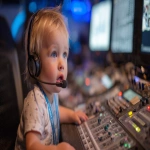 **a baby wearing a clearcom headset and sitting in front of a video switcher, photograph, --ar 16:9** - Image #4 <@960702118686244966>