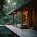 **rich, pronounced 35mm film grain, subtle frame edge softness, authentic Kodak Portra 160 film texture pushed one stop, soft warm-neutral tones with lifted shadows and airy tonal curve, muted greens in foliage, pale stone and light timber surfaces, highlights with gentle halation bloom, gentle color shift in shadows for analog realism, ultra-luxury minimal aesthetic, shot on Hasselblad 500CM with 50mm Distagon lens. Wide shot of a timber-clad sauna pavilion with floor-to-ceiling glass looking into softly lit rainforest. Exterior pale stone decking with a small reflecting pool beside the structure, surface gently rippling. Inside, warm cedar walls glow in the late afternoon light. Soft steam visible against the glass, creating a tranquil, spa-like atmosphere.** - Image #4 <@837237355722571776>