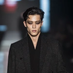 **full-body runway shot of a fashionable 30-year-old Taiwanese man, long-shaped face, fair pale skin, thick eyebrows, large expressive double-lidded eyes, naturally full lips, cheeks softly contoured (not sunken); styled with bold high-fashion smokey eye makeup in deep charcoal and cocoa tones, paired with glossy lip color; contemporary hairstyle with clean lines; walking confidently on a glossy fashion runway under cinematic spotlights, blurred audience and LED backdrop, minimal avant-garde outfit that complements the makeup without distraction; high-contrast editorial lighting, sharp focus on face and makeup while preserving runway motion, premium fashion magazine aesthetic, no text, no watermark --ar 1:1** - Image #4 <@1090872516857299025>
