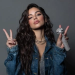**beautiful female with ivory cream skin tone, dark brown eyes shaped like almonds, perfect lip pout, high cheek bones, medium built physique, even and balanced curvy body, long dark brown wavy hair, black eyeliner on eyes catwinged wearing a jean jacket camera catches her from the ground looking up holding her diamond microphone and her other hand holds up the peace sign** - Image #3 <@1097455990200340520>
