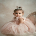 **baby girl styled with an elegant princess bun, smooth brown hair adorned with a tiny silver tiara, wearing a soft pink tulle dress, sitting in a decorative chair Shot with Canon EOS R8, 85mm lens, f/2.0, ISO 100, White Balance 5600K, Portrait Studio Setup --ar 2:3 --v 7.0** - Image #1 <@888546328244801596>