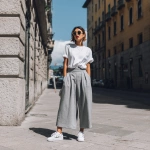 **a woman in grey wide-leg pants, white sneakers, and a t-shirt outfit is standing on the street, wearing the shoes and looking at the camera, with the focus on her legs.** - Image #2 <@1198884420749377556>
