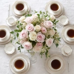 **simple, yet elegant tabletop, view is looking down on it, elegant ivory linen tablecloth, centerpiece of pink and white roses, six (6) steaming coffee cups symmetrically placed at each of the six (6) table settings** - Image #1 <@1141845422852280493>