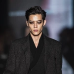 **full-body runway shot of a fashionable 30-year-old Taiwanese man, long-shaped face, fair pale skin, thick eyebrows, large expressive double-lidded eyes, naturally full lips, cheeks softly contoured (not sunken); styled with bold high-fashion smokey eye makeup in deep charcoal and cocoa tones, paired with glossy lip color; contemporary hairstyle with clean lines; walking confidently on a glossy fashion runway under cinematic spotlights, blurred audience and LED backdrop, minimal avant-garde outfit that complements the makeup without distraction; high-contrast editorial lighting, sharp focus on face and makeup while preserving runway motion, premium fashion magazine aesthetic, no text, no watermark --ar 1:1** - Image #3 <@1090872516857299025>