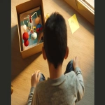 **<https://s.mj.run/KhKr0zYicTk> <https://s.mj.run/xGQrUpUV4sY> Cinematic film still, photorealistic. Over-the-shoulder shot of the same boy from the reference image, sitting on the floor in an empty office room. The camera is just above his shoulder, framing his hands holding an open gift package. Inside the box, a colorful baby mobile with small toys is clearly visible. Next to the package, placed on top of the wrapping paper, is a small yellow post-it note. The boy’s head and shoulder are blurred in the foreground as soft framing, while the focus is on the open box with the baby mobile and the note. Warm golden cinematic lighting, shallow depth of field, subtle film grain. Shot like a high-end Christmas commercial with an Arri Alexa cinema camera --ar 16:9 --v 6.0 --no cartoon, cgi, clutter --raw** - Image #2 <@1072446343324385341>