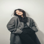 **A Korean woman smile with long hair, wearing an oversized gray woolen coat and black pants. The photography style features white tones, minimalist design, and an elegant posture against a white background. Soft light shines on her face, highlighting its delicate features. --ar 9:16 --v 7.0** - Image #3 <@1136547221920296960>