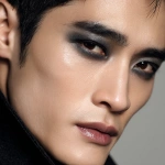 **full-face portrait of a fashionable 30-year-old Taiwanese man, long-shaped face, fair pale skin, thick eyebrows, large expressive double-lidded eyes, and naturally full lips, with softly contoured cheeks not sunken; styled with bold high-fashion smokey eye makeup in deep gray and black tones, paired with glossy lip color for a striking contrast; contemporary hairstyle with clean lines, cinematic editorial lighting highlighting makeup and hair details, blurred neutral background, sharp focus on facial features, refined fashion magazine aesthetic, no text, no watermark --ar 1:1** - Image #3 <@1090872516857299025>