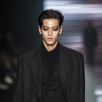 **full-body runway shot of a fashionable 30-year-old Taiwanese man, long-shaped face, fair pale skin, thick eyebrows, large expressive double-lidded eyes, naturally full lips, cheeks softly contoured (not sunken); styled with bold high-fashion smokey eye makeup in deep charcoal and cocoa tones, paired with glossy lip color; contemporary hairstyle with clean lines; walking confidently on a glossy fashion runway under cinematic spotlights, blurred audience and LED backdrop, minimal avant-garde outfit that complements the makeup without distraction; high-contrast editorial lighting, sharp focus on face and makeup while preserving runway motion, premium fashion magazine aesthetic, no text, no watermark --ar 1:1** - Image #1 <@1090872516857299025>