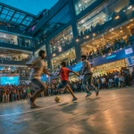 **Young Indian boys and girls playing football on a small 5v5 pitch inside a modern shopping mall, vibrant Premier League branding on boards and banners, a live rap performance on a small stage beside the pitch, energetic crowd of fans filling the upper levels and stands, colorful mall lighting, dynamic motion blur, excited expressions, streetwear outfits, celebratory atmosphere, high-energy urban sports festival vibe, ultra-realistic, cinematic lighting, wide-angle shot. ar16:9** - Image #3 <@1263206055928791131>