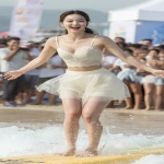 **a joyful Korean university girl with pale glowing skin, camera-facing with a wide smile, standing tall on a surfboard in motion, wearing an ivory sweetheart neckline crop top with lace trims and a translucent soft grey ballet mini skirt, toes visible with soft wet sand, beach crowd cheering behind --v 7.0 --ar 9:16 --q 2 --raw** - Image #2 <@1192072662005059597>