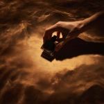 **shadow of masculine hands pulling a small square black glass perfume bottle out of a dark poool of amber colored sensorial oil. The light is diffused and low, revealing texture only in suggestion, not in shine. Every tone sits within a warm spectrum of sienna and tobacco brown. The image feels cinematic and meditative, like the opening frame of a luxury skincare film matte, understated, timeless. ar 21:9 style raw v 6 q 2 uplight low contrast dark tone** - Image #1 <@1137240197814288404>