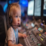 **a baby wearing a clearcom headset and sitting in front of a video switcher, photograph, --ar 16:9 --v 7.0** - Upscaled by <@960702118686244966> (fast)