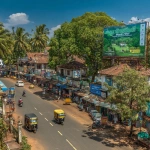 **A busy street scene in Cherthala, Alappuzha, Kerala, India, captured from an elevated angle during a bright sunny day. Lush green trees, traditional Kerala-style buildings with tiled roofs, shops, and colorful vehicles like auto-rickshaws, cars, and motorbikes on the road. A large elevated billboard with a vivid green screen for advertising stands prominently above the street. The scene is full of life and color, realistic lighting, clear blue sky, cinematic composition, ultra-realistic details, 8K, DSLR photo, vibrant urban Kerala atmosphere.** - Image #2 <@1428356262004916394>