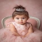 **baby girl styled with an elegant princess bun, smooth brown hair adorned with a tiny silver tiara, wearing a soft pink tulle dress, sitting in a decorative chair Shot with Canon EOS R8, 85mm lens, f/2.0, ISO 100, White Balance 5600K, Portrait Studio Setup --ar 2:3 --v 7.0** - Image #2 <@888546328244801596>