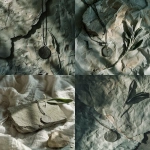 **A minimal editorial photograph of a handcrafted oxidized sterling silver pendant placed on layered textured handmade paper in soft smoke green and mineral grey tones. The surface is irregular, deckled edges visible. Light falls from the upper left as filtered morning light through linen, creating feathered shadows. The pendant features carved angel numbers. No props except a single dried sage leaf placed asymmetrically in the upper right. Composition leaves over 40% negative space. Background texture mimics natural rock sediment in soft detail. --v 6.0** - <@1214240647834509406> (relaxed)