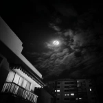 **A photograph of the moon in a black sky, taken from an apartment balcony with a striped, patterned awning and flat white walls, seen through a window of another dark building. The photograph is taken at night. There are some clouds in front of the moon, covering up most of the full moon. It looks like real smartphone footage. --ar 3:4 --raw** - Image #1 <@699706172105556009>