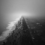 **An evocative and minimalist digital artwork, wide aerial shot, with a dark, monochromatic aesthetic, maintaining the style of the previous designs. The composition depicts a vast, dense crowd of silhouetted figures moving along a narrow strip of land, bordered by a muted, dark sea on one side and a barren, shadowy landscape on the other. The sheer number of individuals creates a sense of overwhelming displacement. The sky is overcast and a uniform dark tone, contributing to a feeling of somberness and uncertainty. The figures appear small and almost indistinguishable, emphasizing the scale of the exodus and their collective vulnerability. The scene evokes a powerful sense of forced migration and the loss of place, rendered with a stark and uncluttered visual style** - Image #1 <@1032195406119043132>