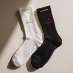 **socks-- one white, one black displayed side-by-side on a clean neutral background, lightweight cotton, modern relaxed fit, subtle Johnnie Walker branding in gold or ruby red, front features small striding man emblem or "Keep Walking", back features bold festival-inspired graphic or quote, soft shadows, merch showcase** - Image #1 <@1323594991586770995>