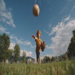 **Image from slightly above eye level: a 10-year-old boy wearing blue shorts and an ochre t-shirt stands on a lush green park lawn, mid-action as he throws a baseball directly toward the viewer. A baseball glove is on his hand, and the ball floats mid-air above him. He is looking directly at the camera. Natural sunlight with soft shadows illuminates the scene. The background features a clear blue summer sky, distant trees, and buildings along the horizon. Full-body view, professional color grading, clean sharp focus, no grain, cinematic quality. Shot with a Sony Alpha A7 III and Zeiss ultra-macro lens, f/2.8 aperture, high resolution:: --aspect 16:9 --s 250 --v 7.0** - Upscaled by <@1220830039520841890> (fast)