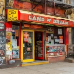 **Photorealistic New York City bodega storefront named "LAND OF DR3AMS", classic NYC corner store exterior, red and yellow color scheme, awning and signage reading: "L A N D O F D R 3 A M S" (the word DR3AMS uses the number 3, not the letter E), authentic five-borough bodega atmosphere, glass windows with posters and signs, metal gate partially visible, sidewalk perspective, gritty but warm urban realism, lived-in neighborhood feel, not hand-painted, printed storefront sign, real New Yorker energy, cultural authenticity, no corporate branding, no chain store look. --ar 3:4 --v 6.0 --raw** - Image #2 <@1202283570215788544>