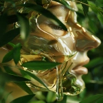 **Abstract skincare ad, close-up of a human face made entirely of clear, reflective glass, surrounded by fresh green leaves, golden face oil slowly dripping and flowing down the smooth glass surface, hyper-realistic textures, soft natural lighting, ethereal and artistic, luxury beauty campaign, minimalist studio background --ar 3:4 --v 6.0 --raw** - Image #3 <@1137663032605028362>