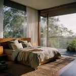 **Captured by a world-class luxury architectural and interior photographer, renowned for editorial storytelling and natural light mastery rich, pronounced 35mm film grain, subtle frame edge softness, authentic Kodak Portra 160 film texture pushed one stop, halation bloom on highlights, gentle color shift in shadows for analog realism, shot on Hasselblad 500CM ultra-luxury minimal master bedroom seamlessly blending with nature. Floor-to-ceiling glass opens to a private balcony overlooking lush treetops of the Queensland hinterland. King bed with low timber headboard in warm washed oak, dressed in natural Belgian linen with muted cream and soft grey tones. Textured jute rug underfoot, sculptural bedside lamps with soft warm glow. Early morning light filtering through sheer curtains, lifted shadows, soft highlights, warm neutral tones, balanced whites. Composition centered, allowing symmetry between interior and landscape, editorial architectural photography.** - Image #4 <@837237355722571776>