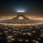 **A breathtaking cinematic night scene in Tehran. A massive, peaceful crowd surrounds the Azadi Tower in complete darkness. Thousands of people hold up their phones, creating a sea of warm white lights forming a perfect circle around the monument. The Azadi Tower stands in the center, monumental, softly illuminated, calm and timeless. No faces visible, only silhouettes unity over individuality. Atmosphere is silent, emotional, sacred, and powerful. Subtle mist in the air, deep shadows, dramatic contrast. Ultra-realistic photography, cinematic lighting, long exposure look, high detail. Shot from a high aerial perspective, epic scale. Mood: hope, resilience, quiet strength, goosebumps. --ar 9:16** - Image #3 <@1243161661557309564>
