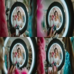 **A medium shot of a stylish Western female fashion influencer livestreaming, actively holding a white lace blouse against her body to demonstrate the fit, her hands are visible gripping the hanger and touching the fabric details to showcase the texture. She has an exaggerated shocked and excited expression with her mouth open. In the foreground, a blurred silhouette of a ring light and smartphone recording the scene. Background features a rack of colorful clothes. High energy, commercial livestream photography, sharp focus on the influencer and the clothing, with high detail ,photograph --ar 16:9** - Zoom Out by <@950232969275125781> (fast)