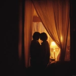 **A romantic couple sharing an intimate moment behind soft golden curtains, warmly lit by a cozy floor lamp, wrapped together in a blanket, silhouetted gently, dreamy and tender atmosphere, early morning or twilight glow, peaceful indoor setting, shallow depth of field, cinematic lighting, vintage color grading, 35mm film style, subtle grain, emotional storytelling, soft focus, style cinematic** - Image #1 <@1331627685406965792>