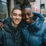 **two handsome young men smiling, one is white with short brown hair and the other has black skin and long, curly topknot hairstyle wearing an oversized, puffy blue jacket. both of them are hugging each other in love on a street corner. photo-realistic, portrait photography, in the style of nikon d850. --ar 127:128 --v 7.0 --p 7t8d38w** - Image #3 <@995751013732581408>