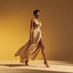 **A powerful fashion editorial image of a confident woman walking gracefully across a smooth, minimal golden-yellow gradient background. She wears a flowing, satin high-slit dress in champagne or ivory tones, paired with stylish high heels. The lighting is dramatic and cinematic, casting soft shadows on the ground. The setting is studio-lit, ultra-clean, with a fashion-forward, luxury tone. Shot in full-body, side profile, high resolution, editorial style, Vogue aesthetic.** - Image #3 <@1323594991586770995>