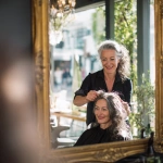 **a smiling female hairdresser in her early forties is standing arranging the hair of a client in a beauty salon facing the large mirrors, beside the windows that give on a lovely street full of green treas. It's a beautiful day and the warm sunlight enters the beauty salon through the windows, 35 mm, realistic, --s 50 --v 7.0 --raw** - Image #4 <@1088739679458824253>