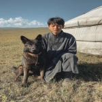 **<https://s.mj.run/o_yLqhTb4aU> <https://s.mj.run/6fMYZkMLVic> A teenage boy sitting next to a dark-colored German Shepherd dog near a traditional Mongolian yurt on grassland, wearing traditional Mongolian casual clothing, the dog wearing a red collar around the dog's neck similar to reference image, scattered wildflowers on the prairie, shot with iPhone camera, midday lighting, natural sunlight, portrait photography, vertical composition --iw 1.5 --v 7.0 --ar 2:3** - Image #2 <@366883290000392193>