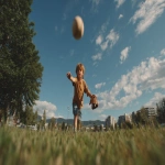 **Image from slightly above eye level: a 10-year-old boy wearing blue shorts and an ochre t-shirt stands on a lush green park lawn, mid-action as he throws a baseball directly toward the viewer. A baseball glove is on his hand, and the ball floats mid-air above him. He is looking directly at the camera. Natural sunlight with soft shadows illuminates the scene. The background features a clear blue summer sky, distant trees, and buildings along the horizon. Full-body view, professional color grading, clean sharp focus, no grain, cinematic quality. Shot with a Sony Alpha A7 III and Zeiss ultra-macro lens, f/2.8 aperture, high resolution:: --aspect 16:9 --s 250 --v 7.0** - Upscaled by <@1220830039520841890> (fast)